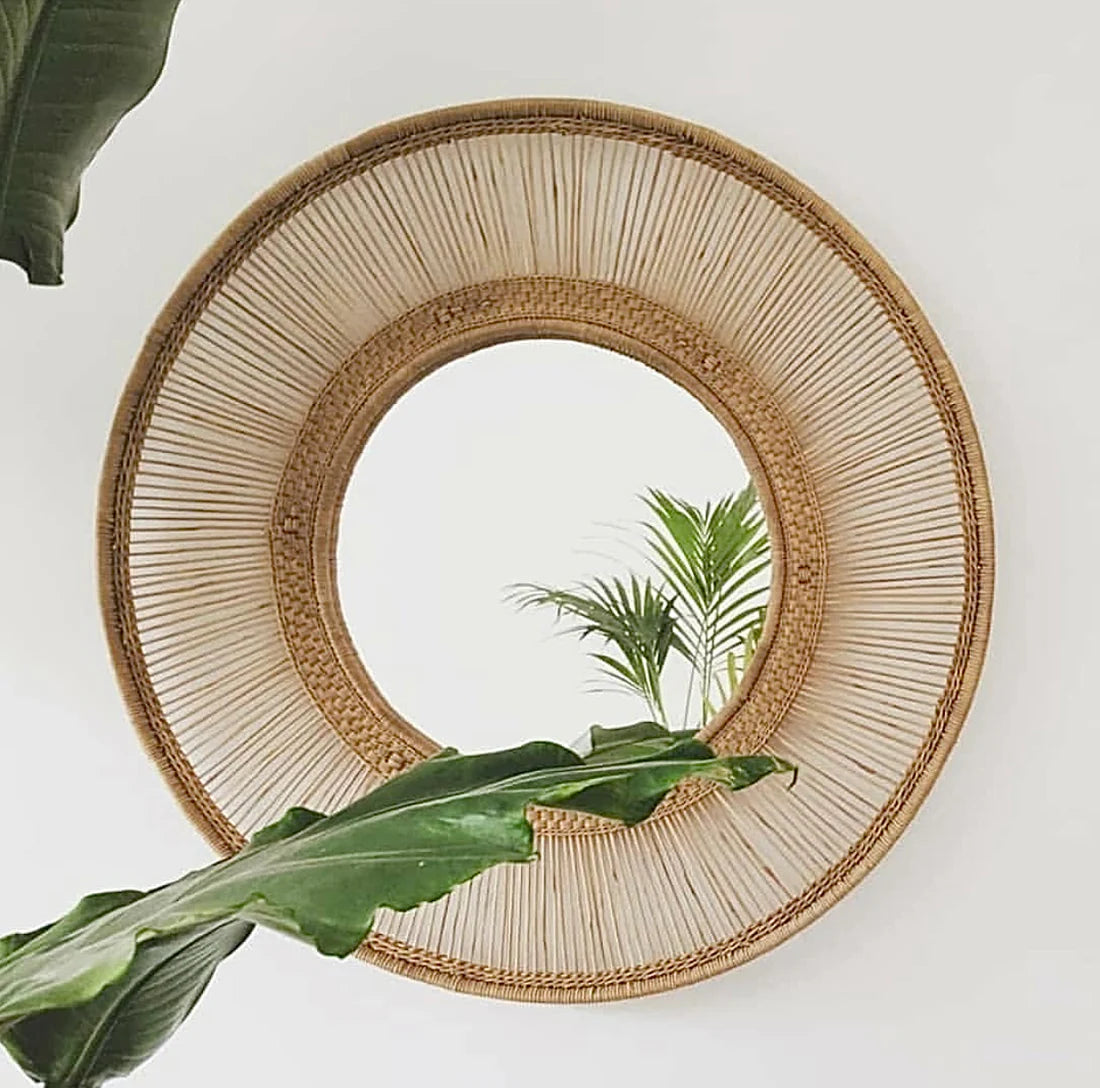 Handwoven circular cane mirror with intricate detailing, enhancing light and space in any room, surrounded by greenery.