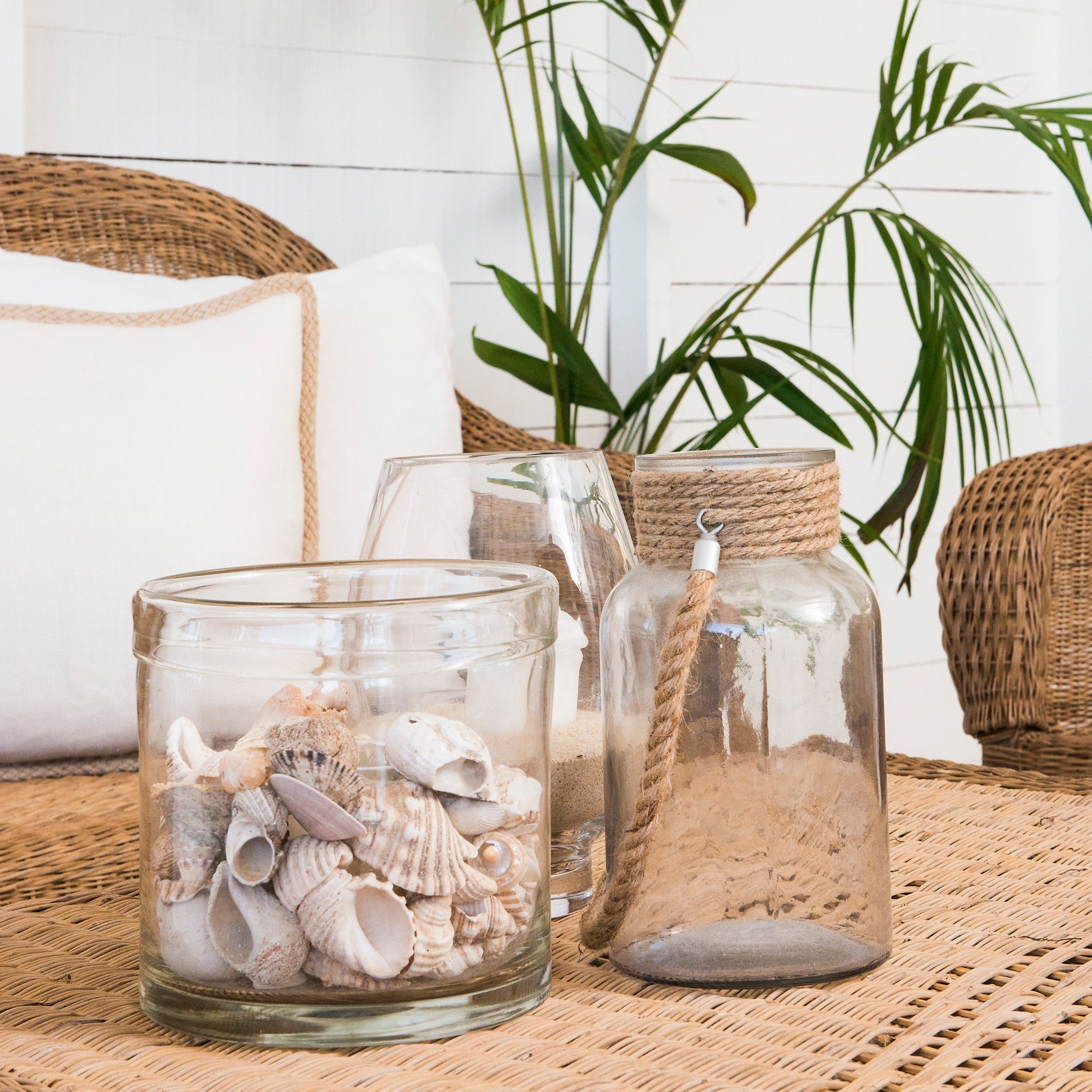 Decorative glass jars with shells on a woven table, palm leaves in the background