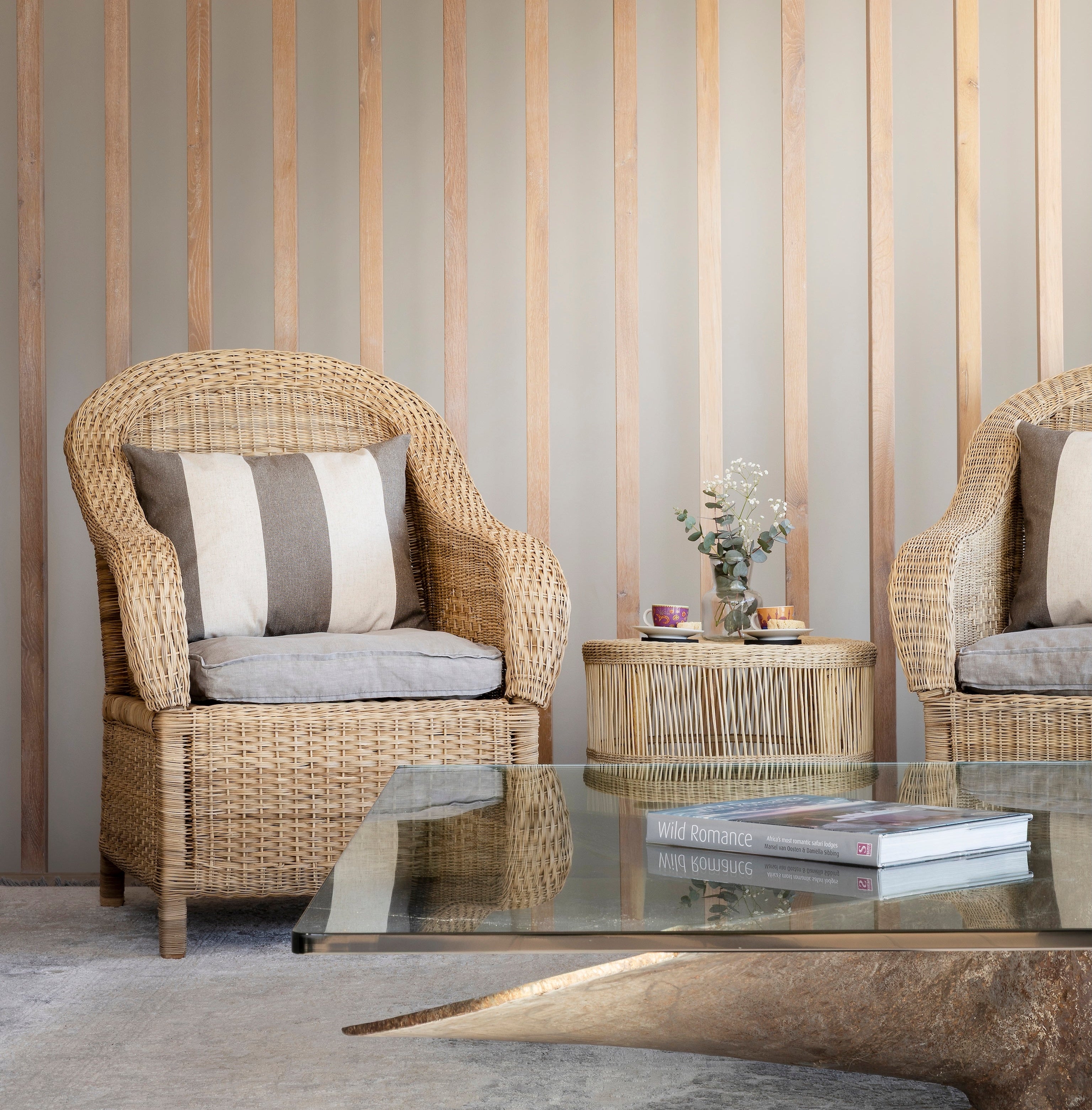 Wicker armchairs with cushions in a room with striped wallpaper.
