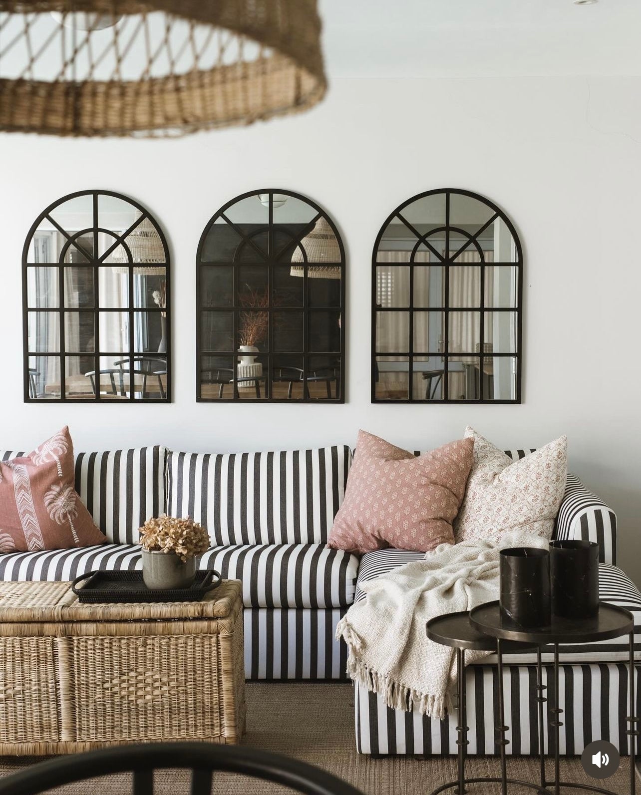 Stylish living room with striped sofa, decorative pillows, handwoven cane storage box, and arched mirrors on the wall.