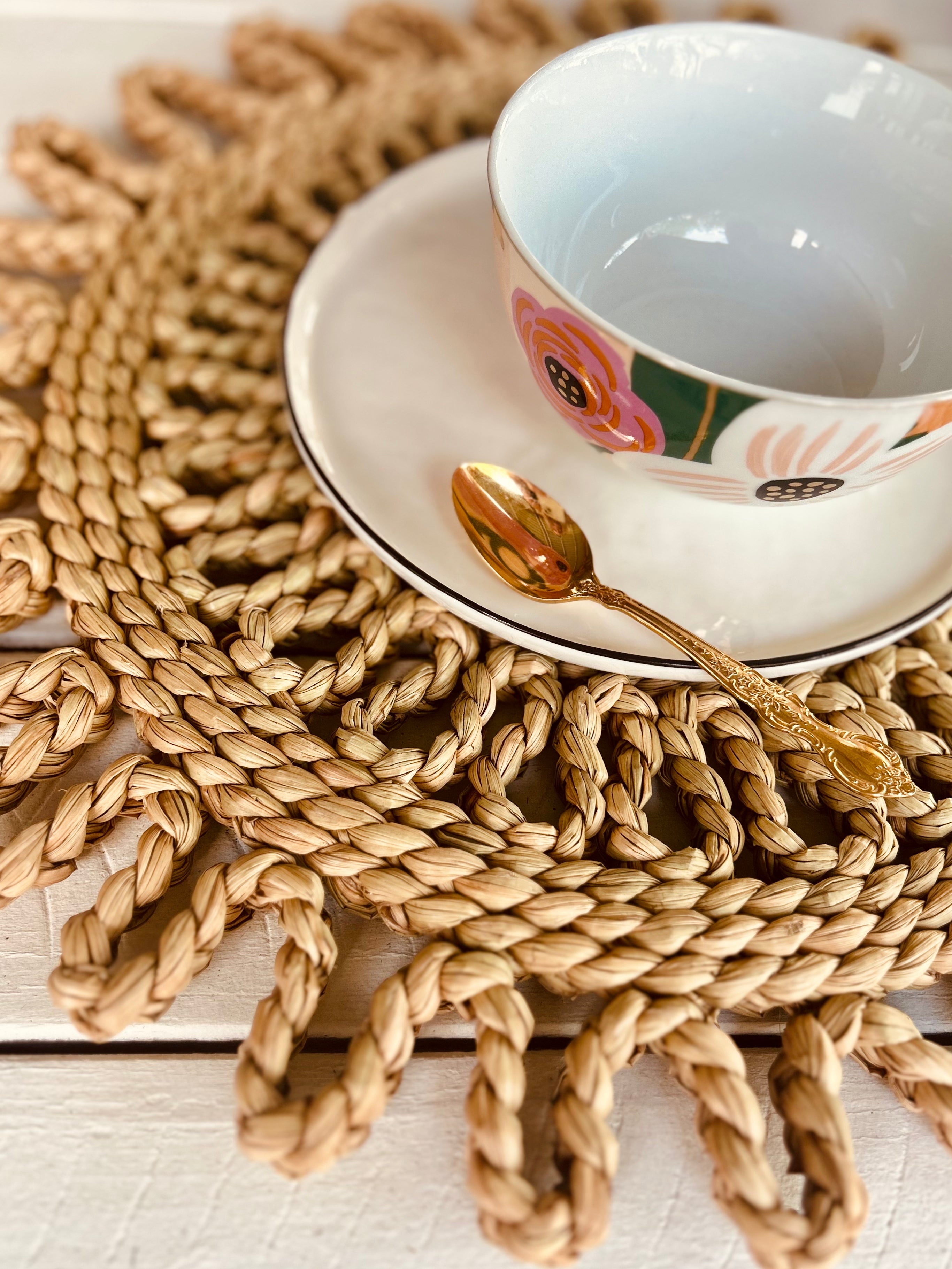 Handwoven rattan scalloped placemat with a decorative bowl and gold spoon, perfect for dining and beach picnics.