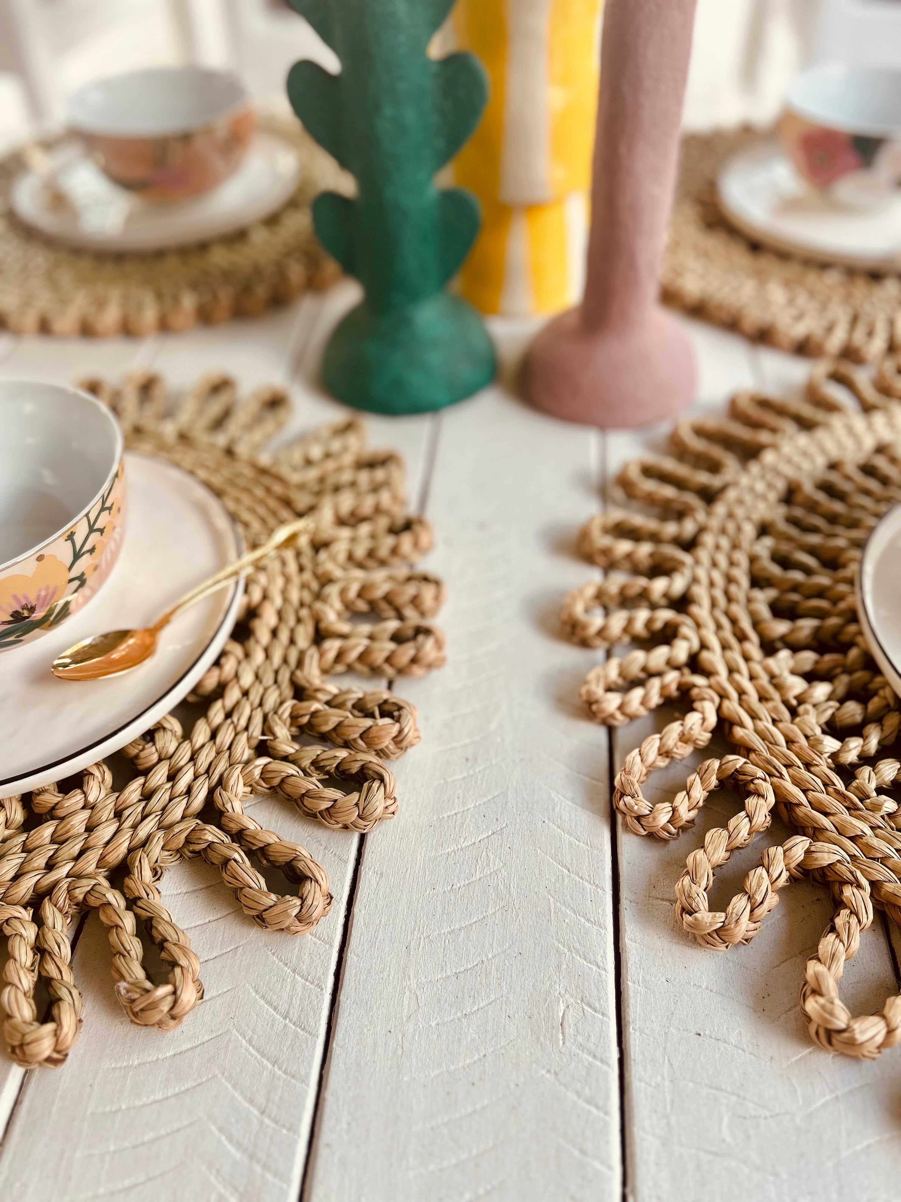 Handwoven scalloped placemats on a dining table setting with bowls and colorful candles, enhancing a warm table atmosphere.