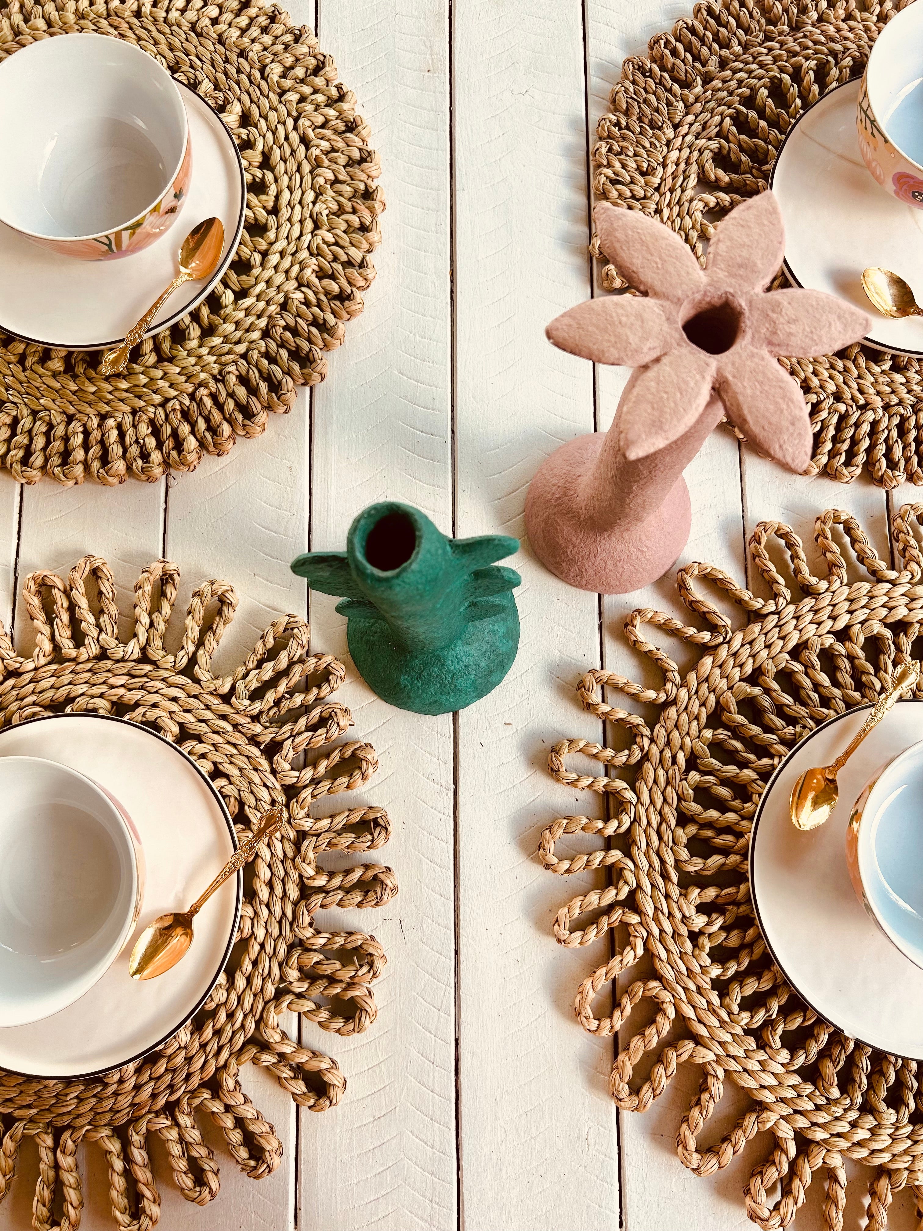 Top view of handwoven placemats with elegant teacups and decorative vases on a rustic wooden table setting.