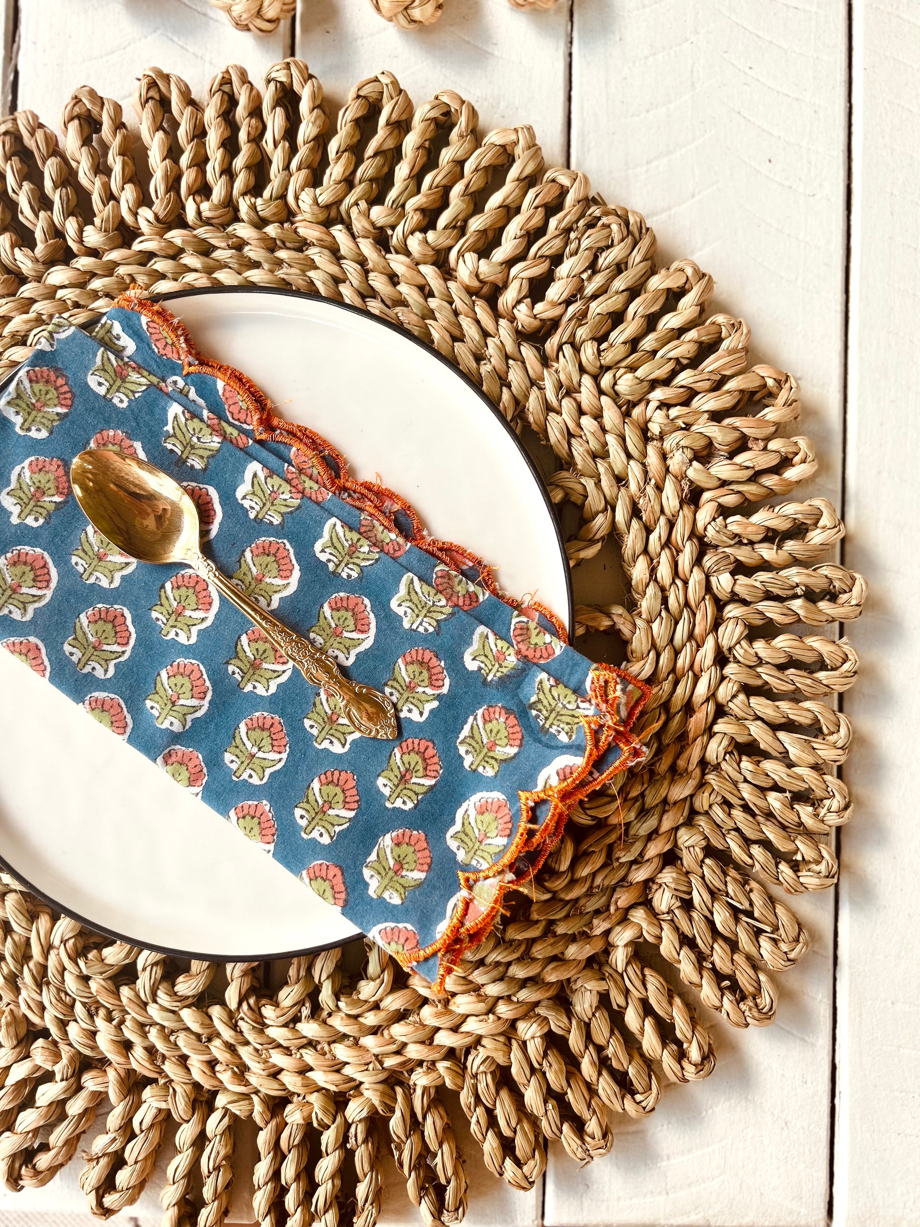 Handwoven scalloped placemat with a plate and shell-patterned napkin, perfect for dining settings or beach picnics.