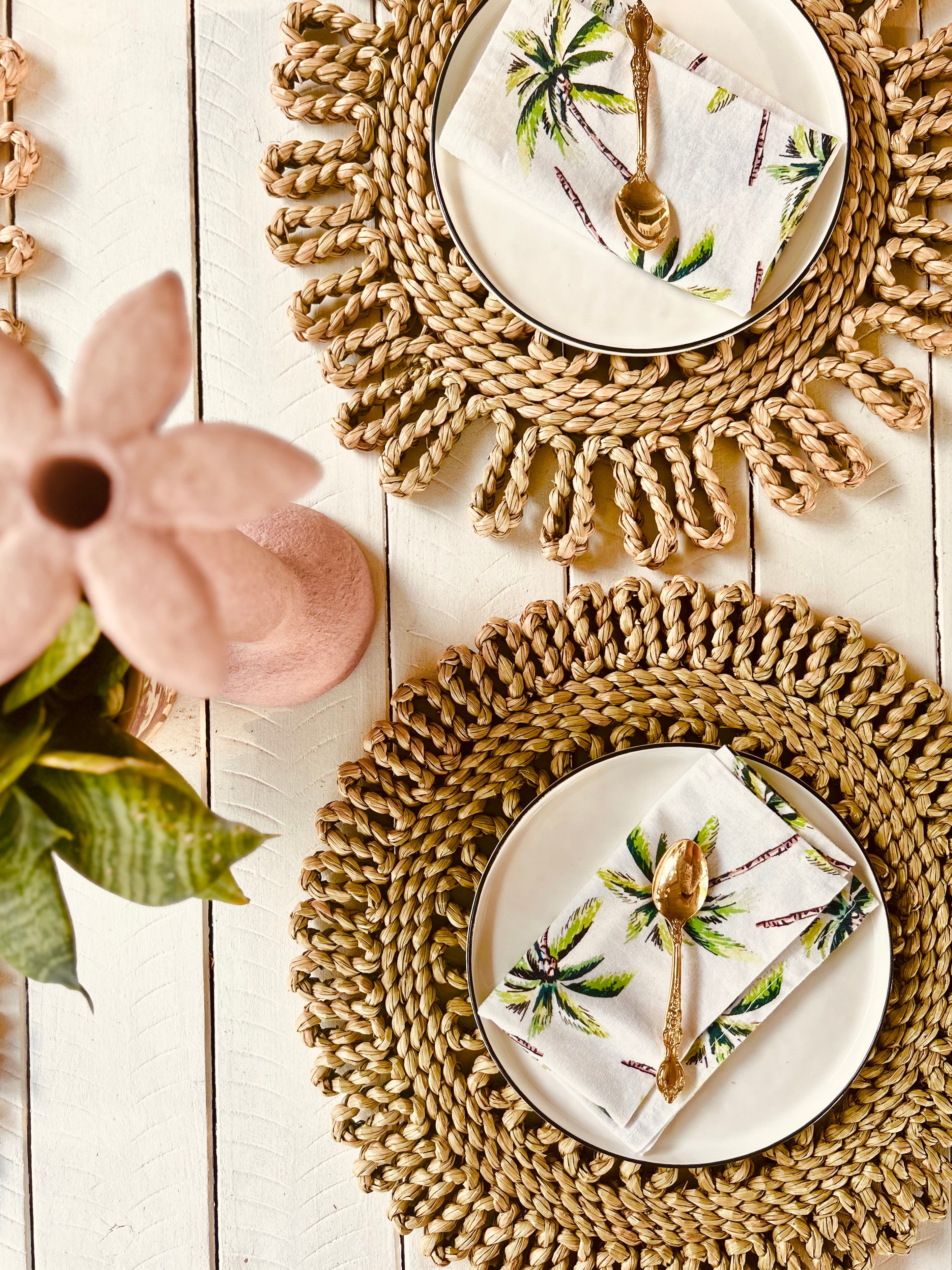 Handwoven rattan scalloped placemats with tropical napkins and cutlery on a wooden table, perfect for beach picnics or dining.