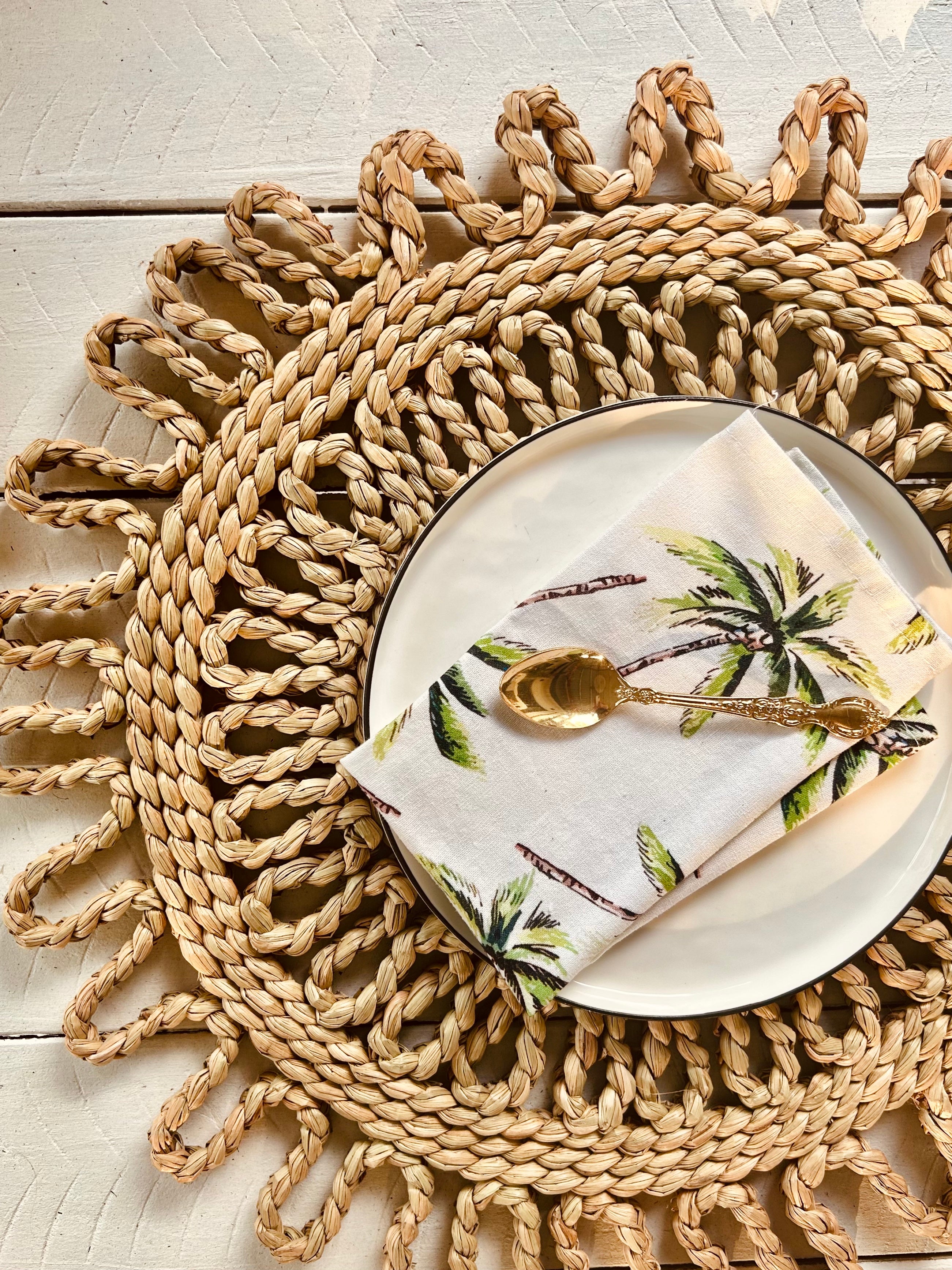 Handwoven scalloped placemat with a plate and palm tree napkin, perfect for beach and picnic dining.