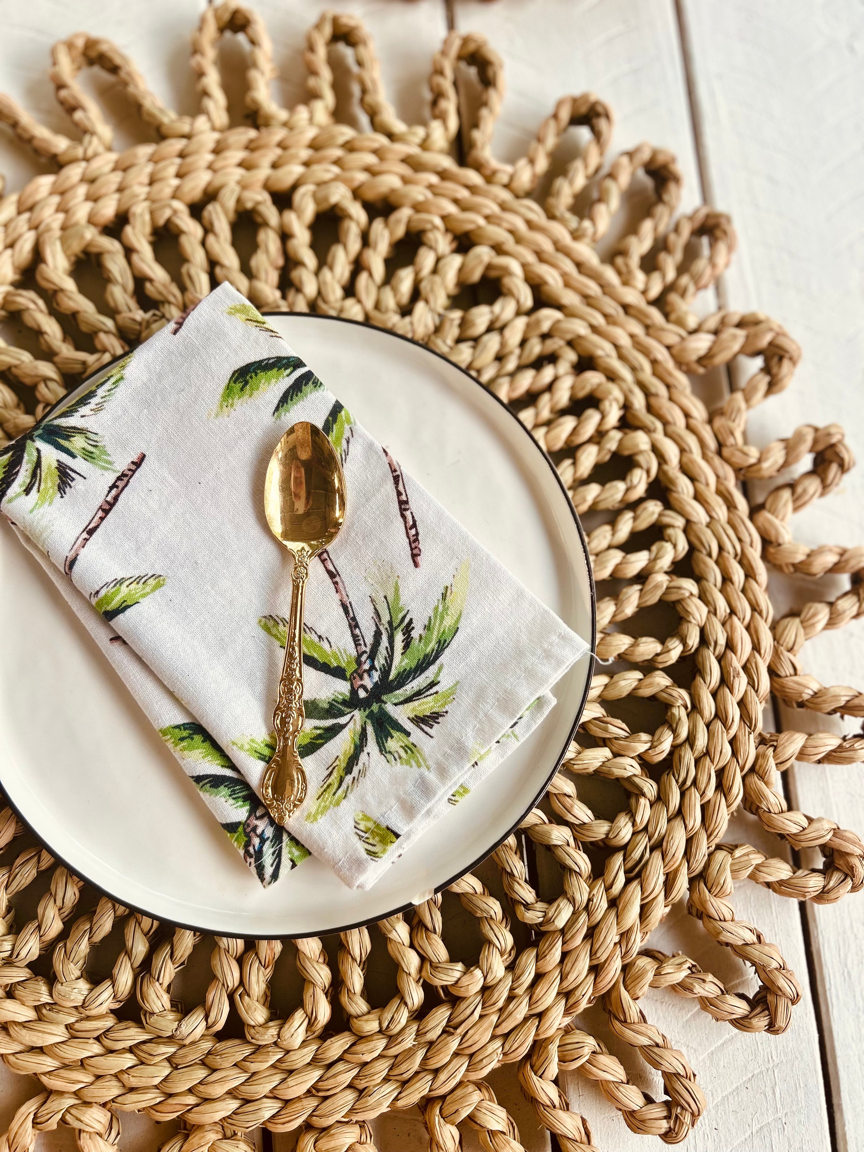 Handwoven scalloped rattan placemat with a white napkin and golden spoon, perfect for beach-themed dining.