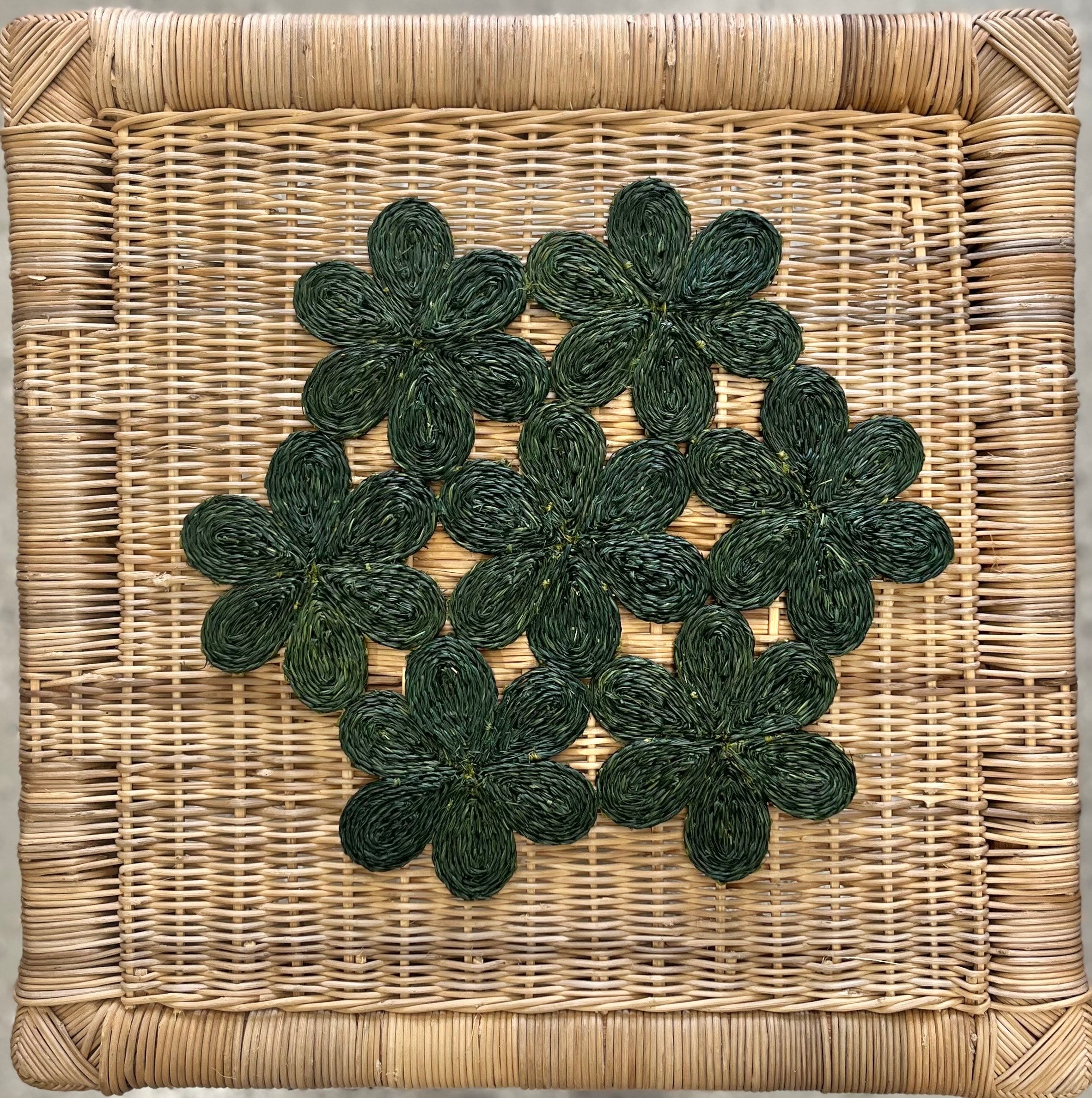Handwoven green floral placemats on a cane basket, perfect for dining, picnics, or beach days.