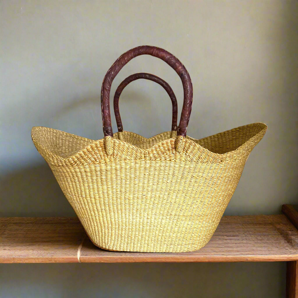Handwoven cane basket with leather handles, perfect for picnics or beach days, showcasing unique organic curves.
