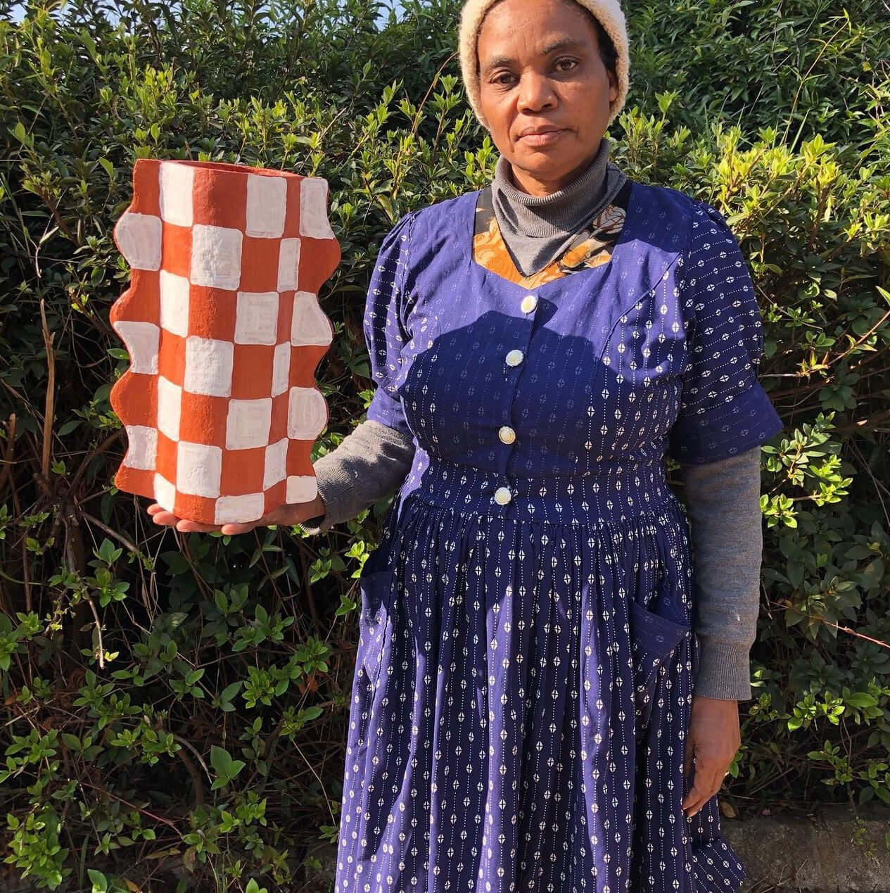 Woman holding a handcrafted pulp mache terracotta Mude Vase with a checked pattern, surrounded by greenery. Perfect for decor or dried flowers.