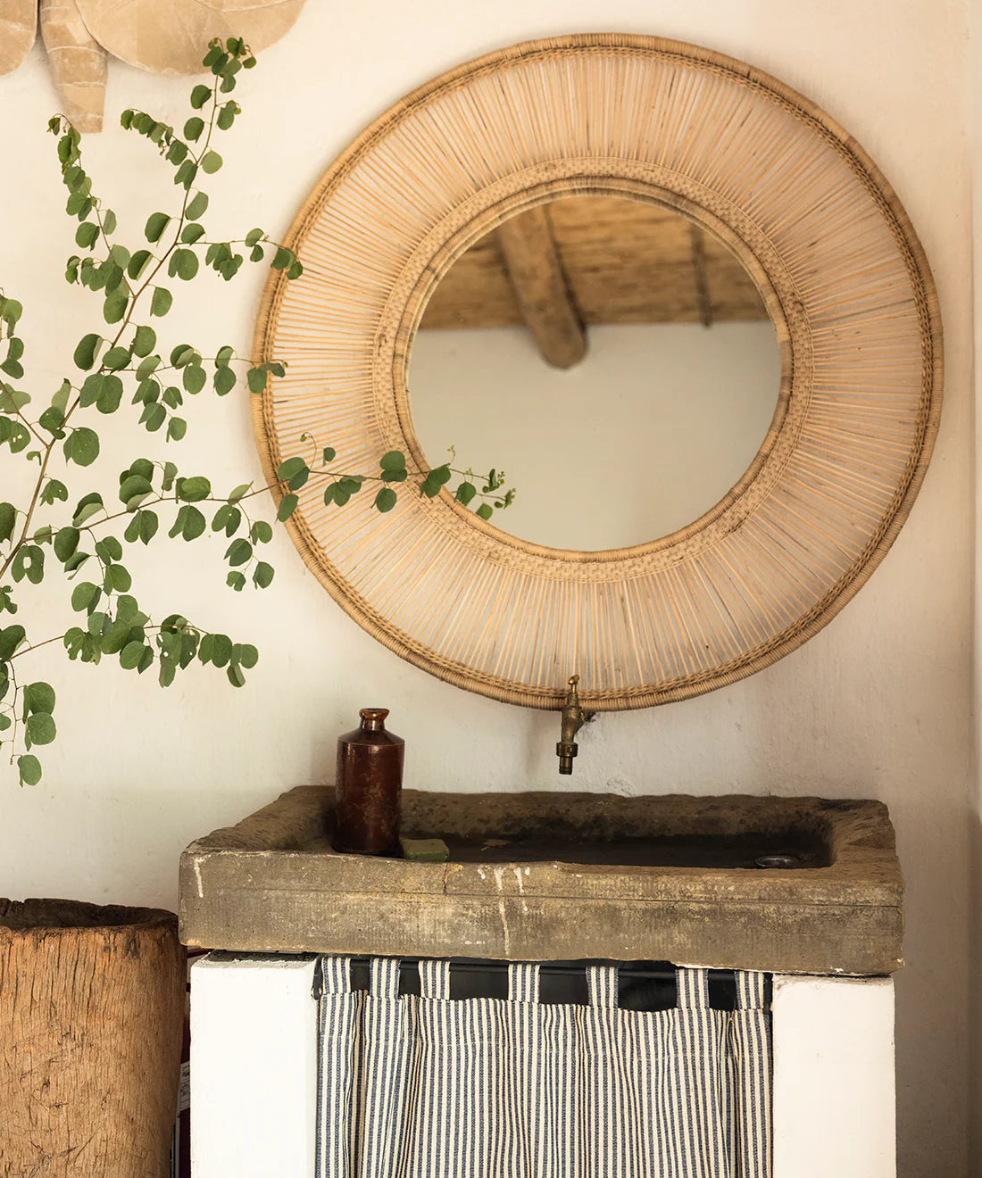 Traditional handwoven cane mirror above a rustic stone sink, enhancing the room's light and space with natural elegance.