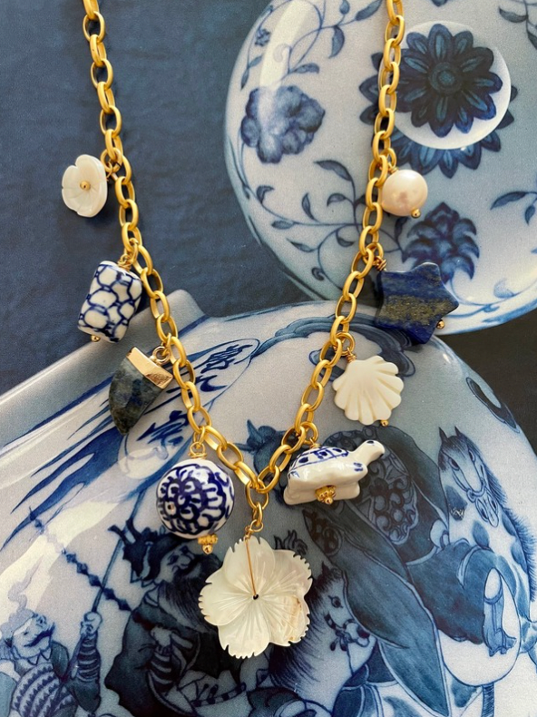 Handcrafted ocean-inspired Jasmine Charm Necklace featuring pearls and porcelain on a gold-plated chain, displayed on blue ceramics.