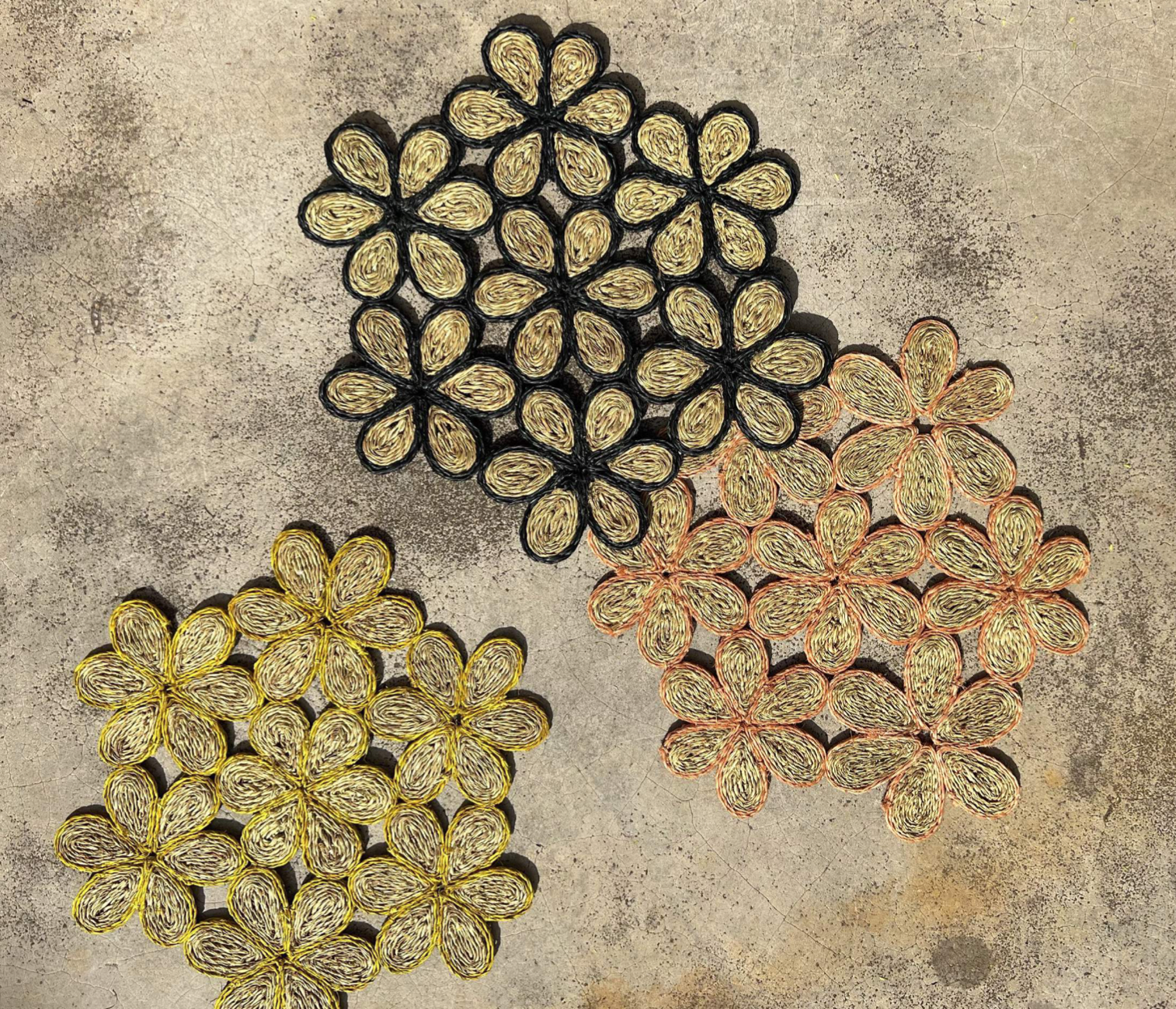 Handwoven floral inspired placemats in black, yellow, and peach, perfect for dining tables and beach picnics.
