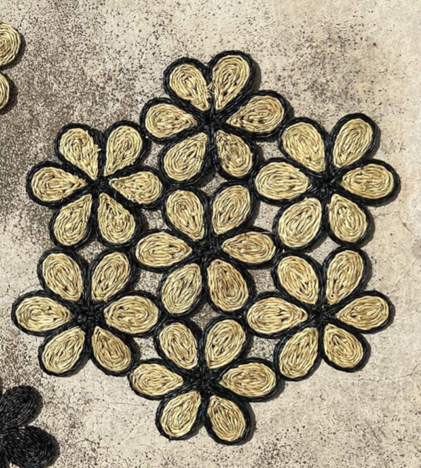 Handwoven floral placemat in black and natural tones, perfect for dining, picnics, or beach outings.