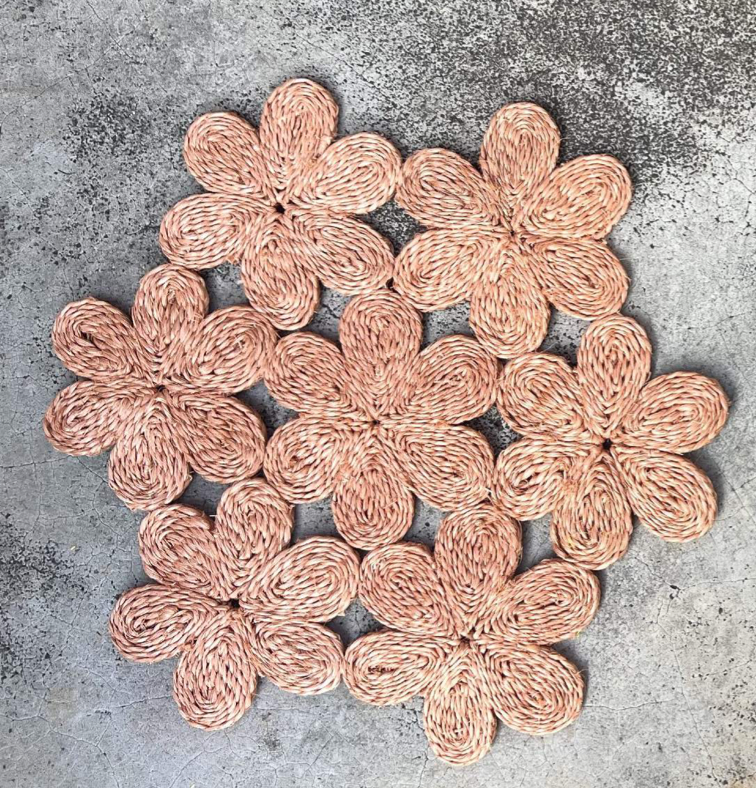 Handwoven floral inspired placemat featuring delicate pink flowers, perfect for dining tables or beach picnics.