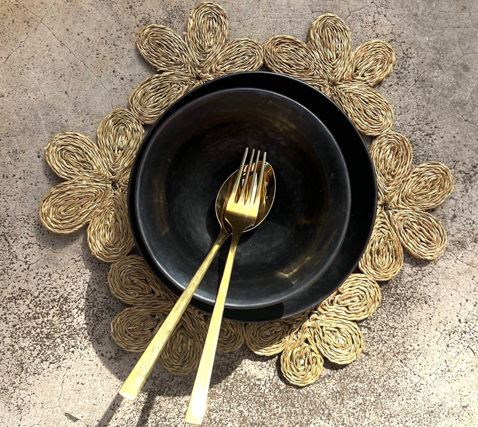 Handwoven floral-inspired placemat with a black bowl and gold utensils, perfect for dining or beach picnics.