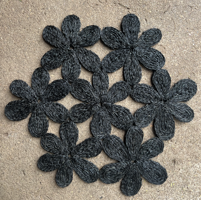 Handwoven black floral placemat, inspired by nature, perfect for dining tables and beach picnics.