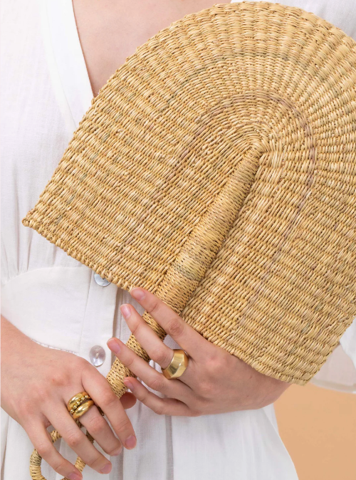 Close-up of a person holding a woven straw bag with gold rings on fingers.