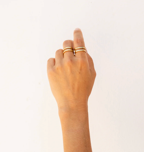Hand wearing two gold rings on a light background