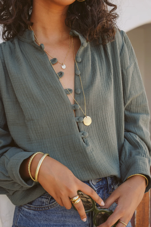 Person wearing a green shirt with buttons, gold necklace, and rings.