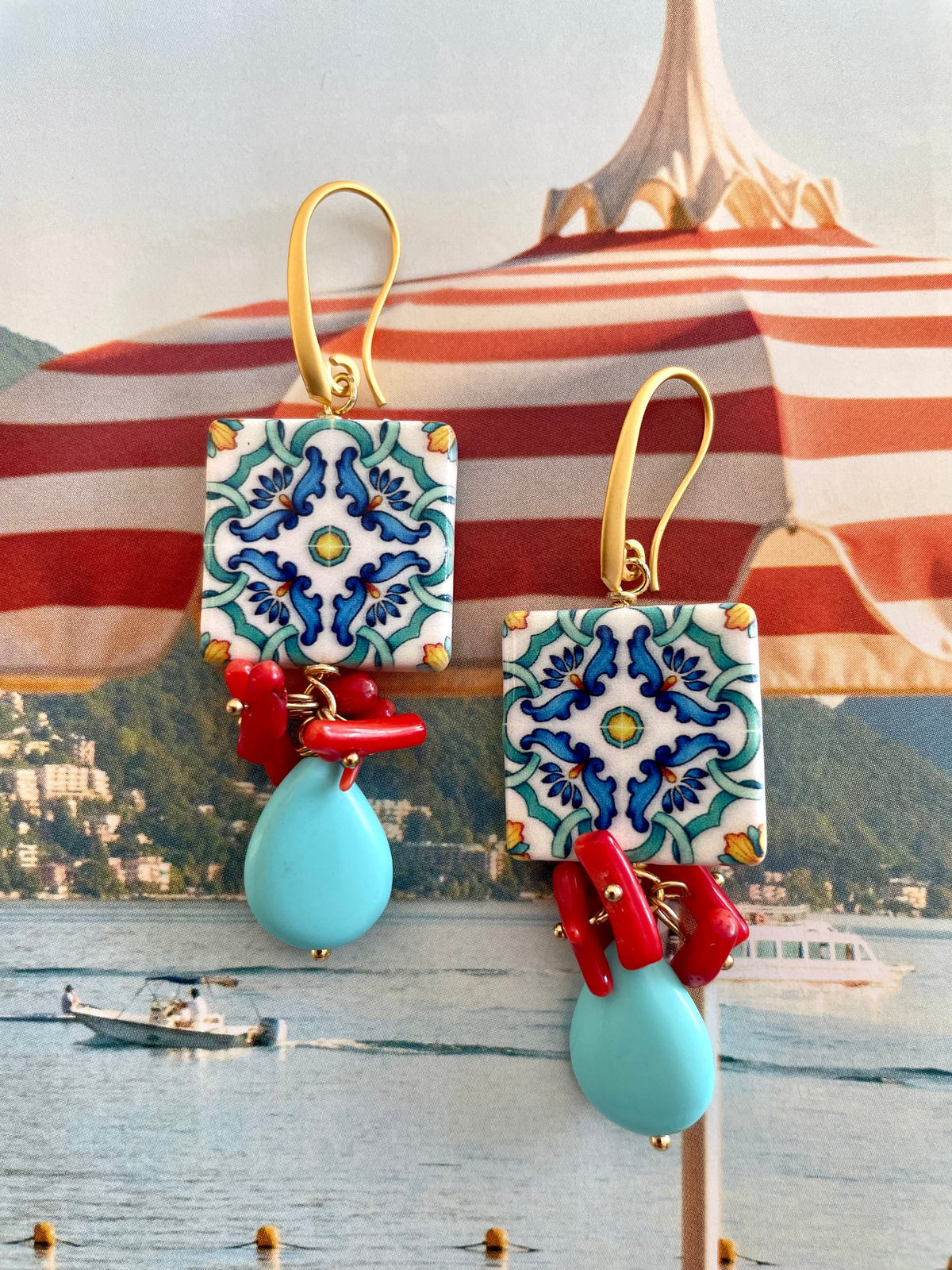 Handcrafted ocean inspired Del Vento Earrings with turquoise and coral charms on a serene seaside background.