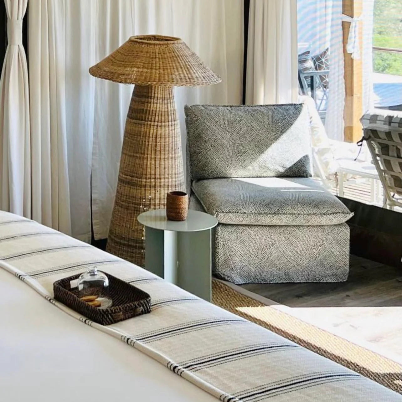 Intaba Cane Woven Floor Lamp beside a cozy seating area, adding a warm glow to a stylish interior with natural textures.