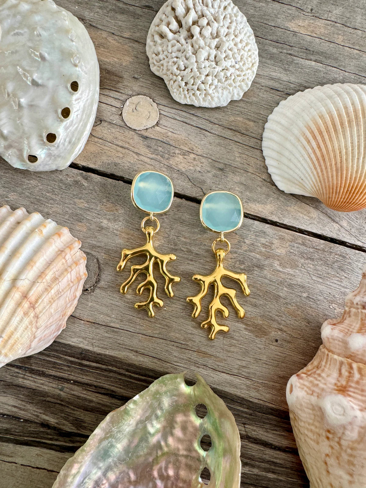 Handcrafted ocean-inspired Lampedusa Earrings featuring gold-plated brass and aqua stone, set on a shell background.