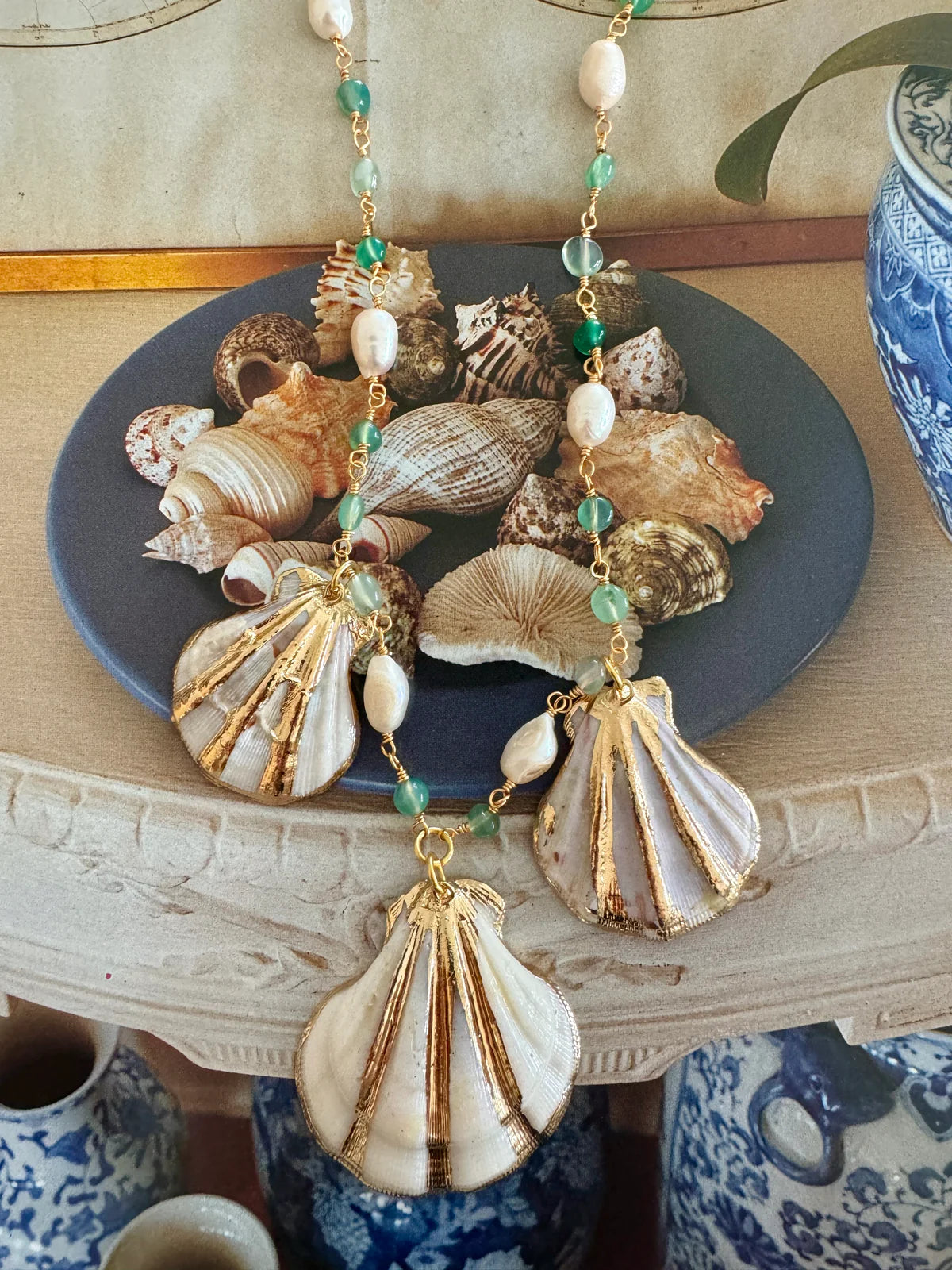 Handcrafted ocean inspired Sapore di Mare Necklace with gold shells, jade, and freshwater pearls on a decorative shell plate.