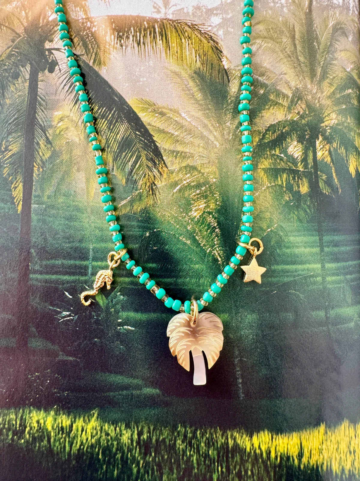 Handcrafted ocean-inspired teal necklace with Mother of Pearl palm tree, sea horse, and star charms.
