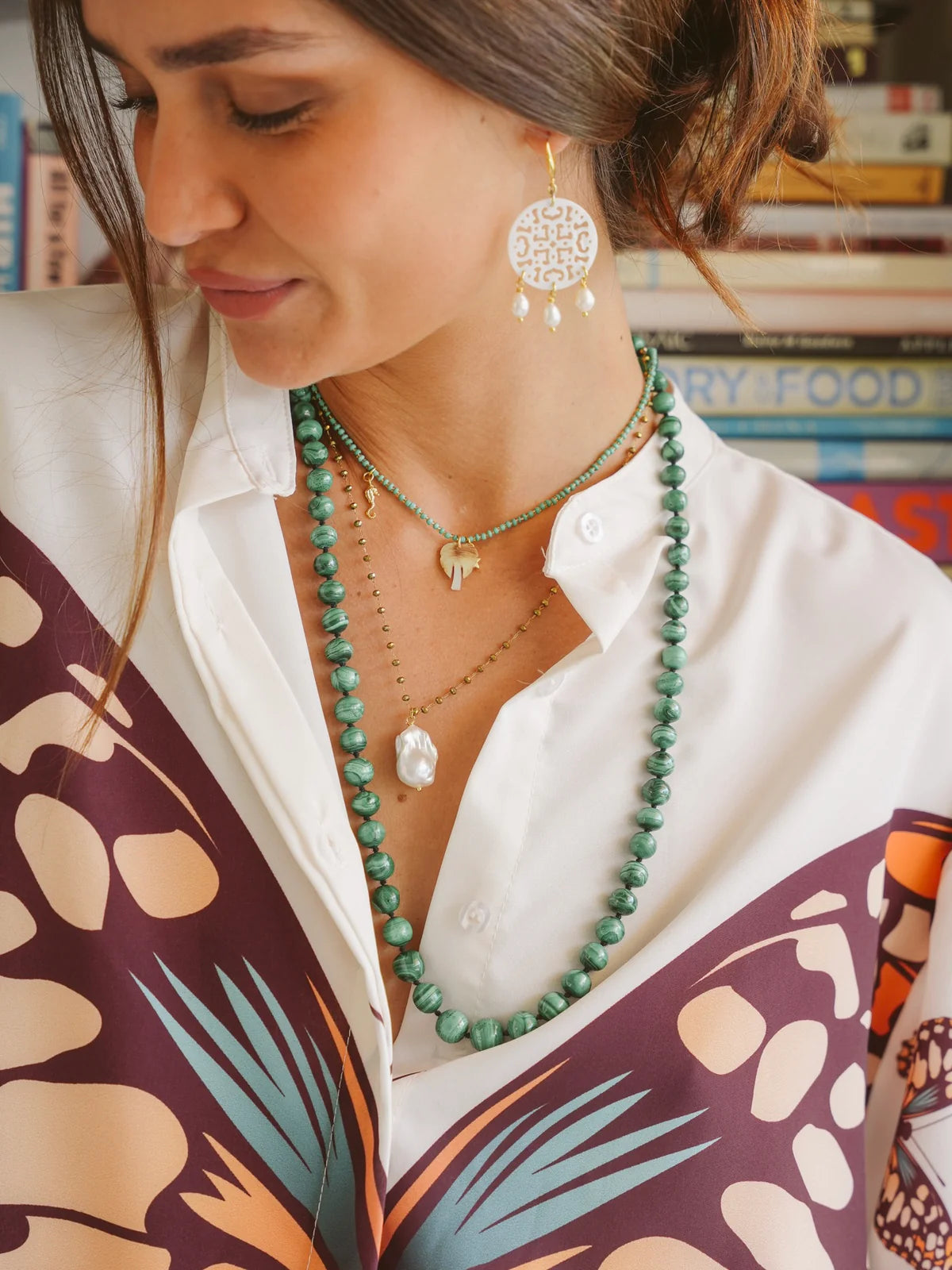 Woman wearing handcrafted ocean inspired teal necklace with charms, styled with a colorful blouse and earrings.