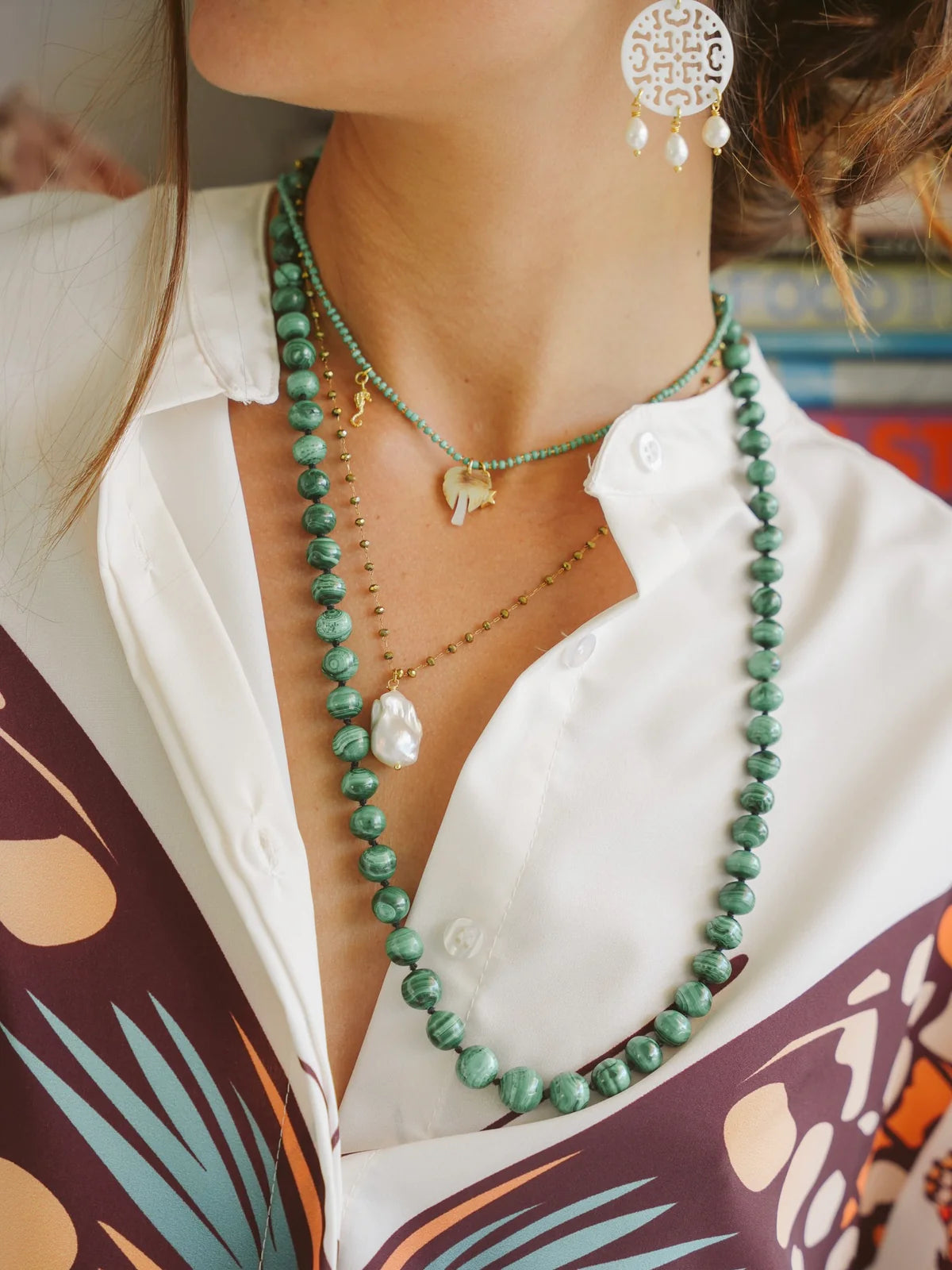 Handcrafted ocean-inspired teal necklace layered with gold and pearl charms, worn with stylish shirt and earrings.