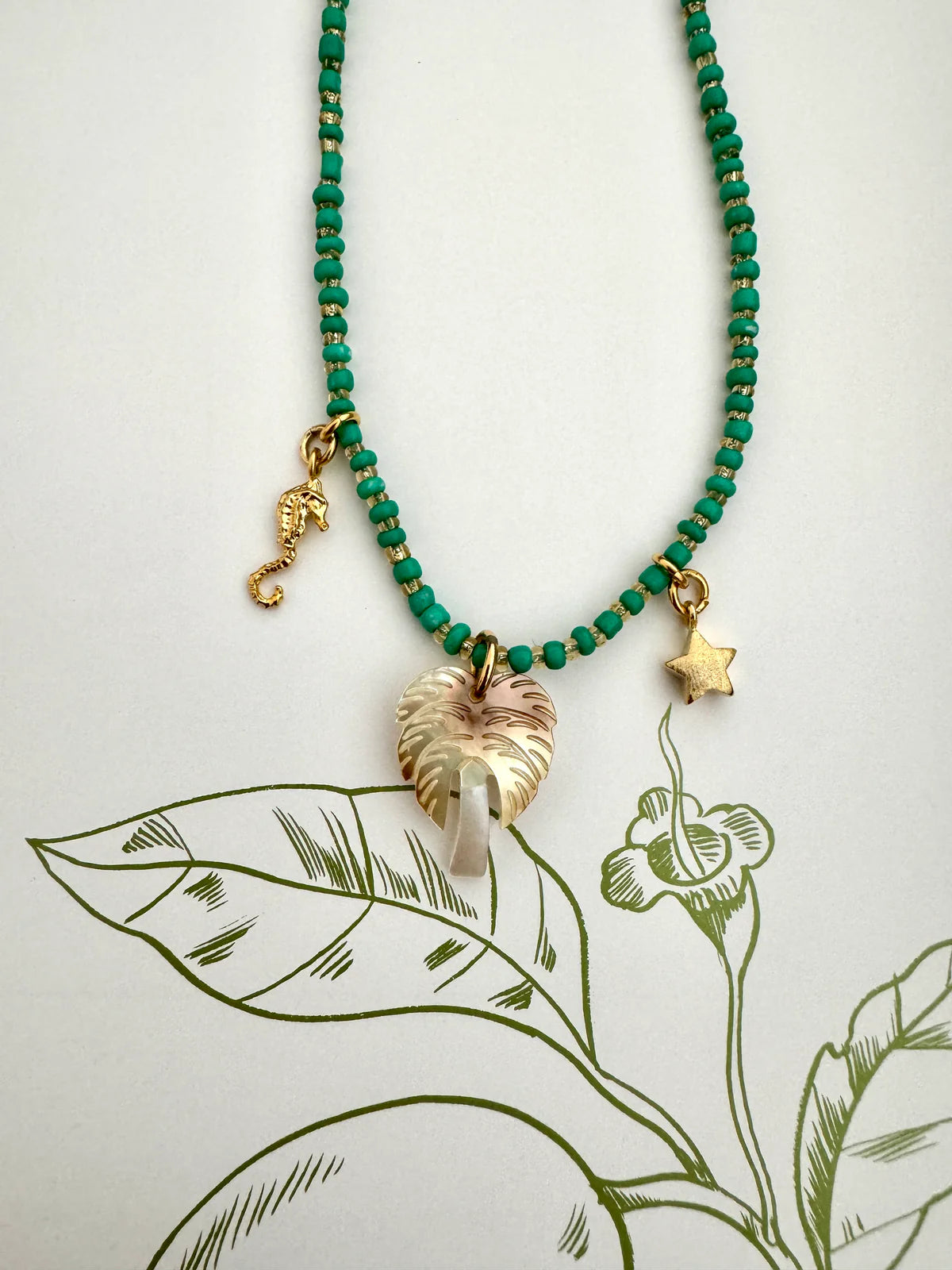 Handcrafted ocean inspired necklace featuring teal glass beads, palm tree pendant, seahorse, and star charms.