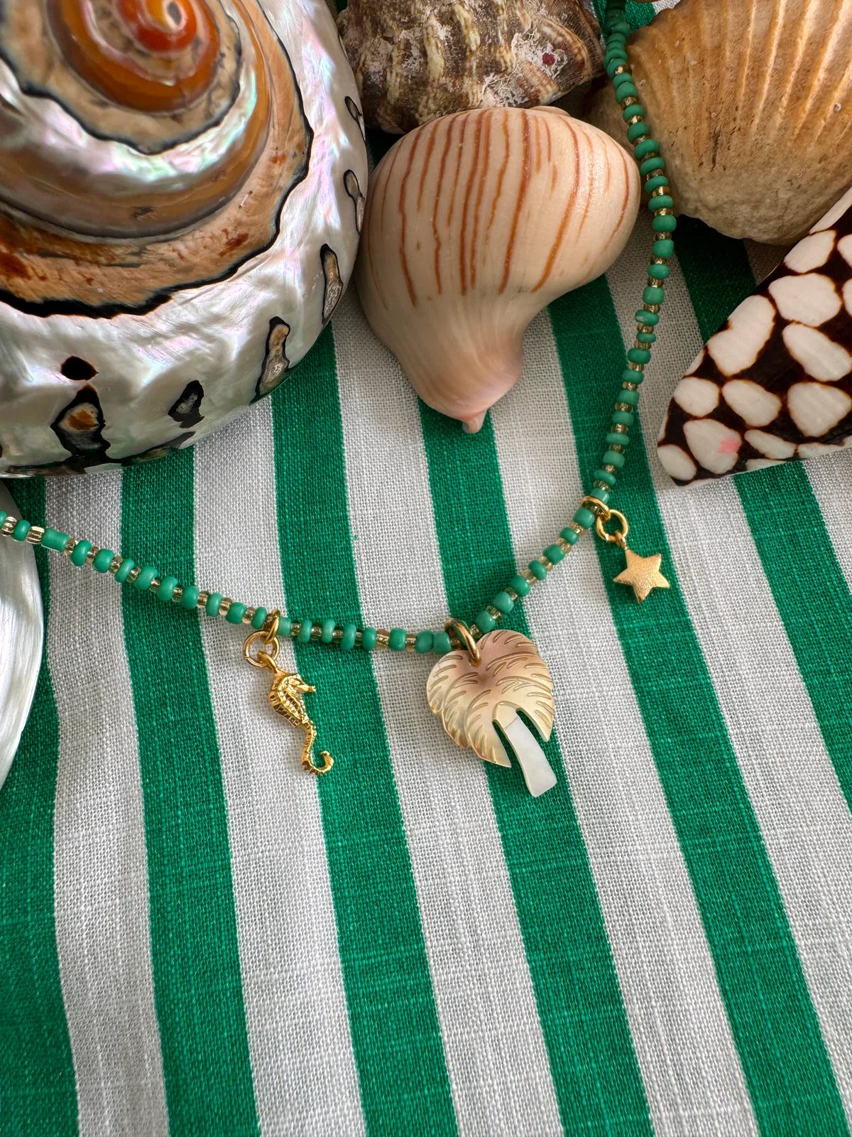 Handcrafted ocean inspired teal souvenir necklace with palm tree, seahorse, and star charms on a striped background.