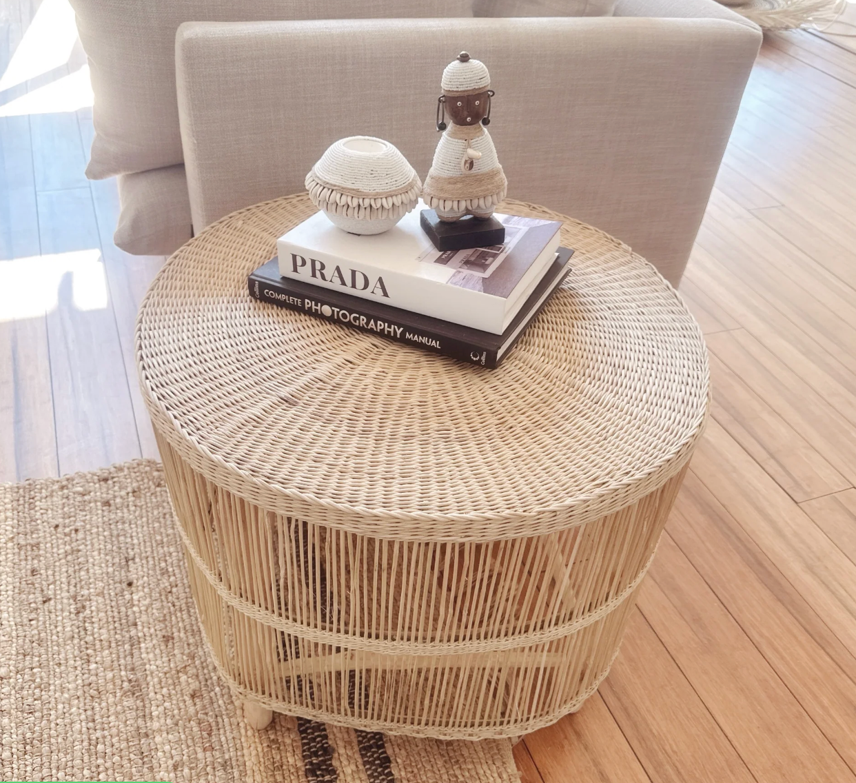 Round wicker side table with decorative items on a wooden floor.