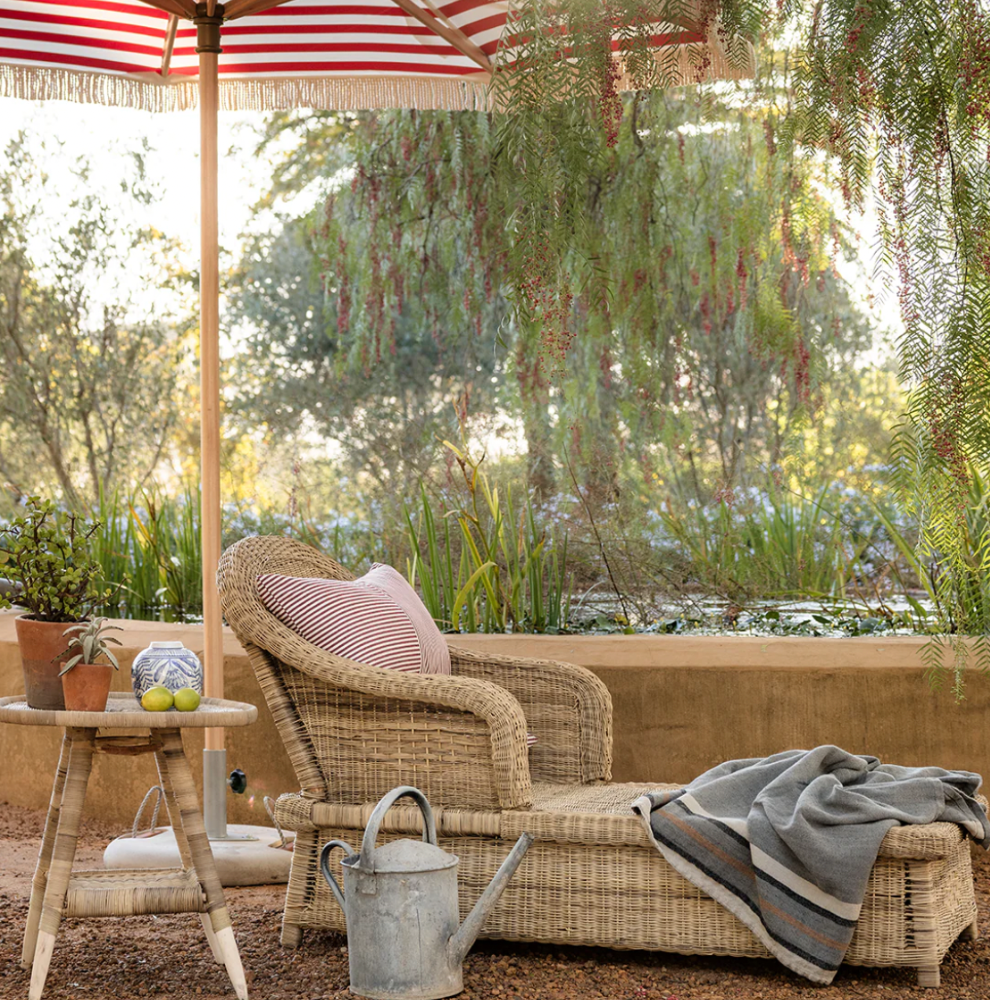 Outdoor setting with Coastal drift cane lounger, striped umbrella, and garden element