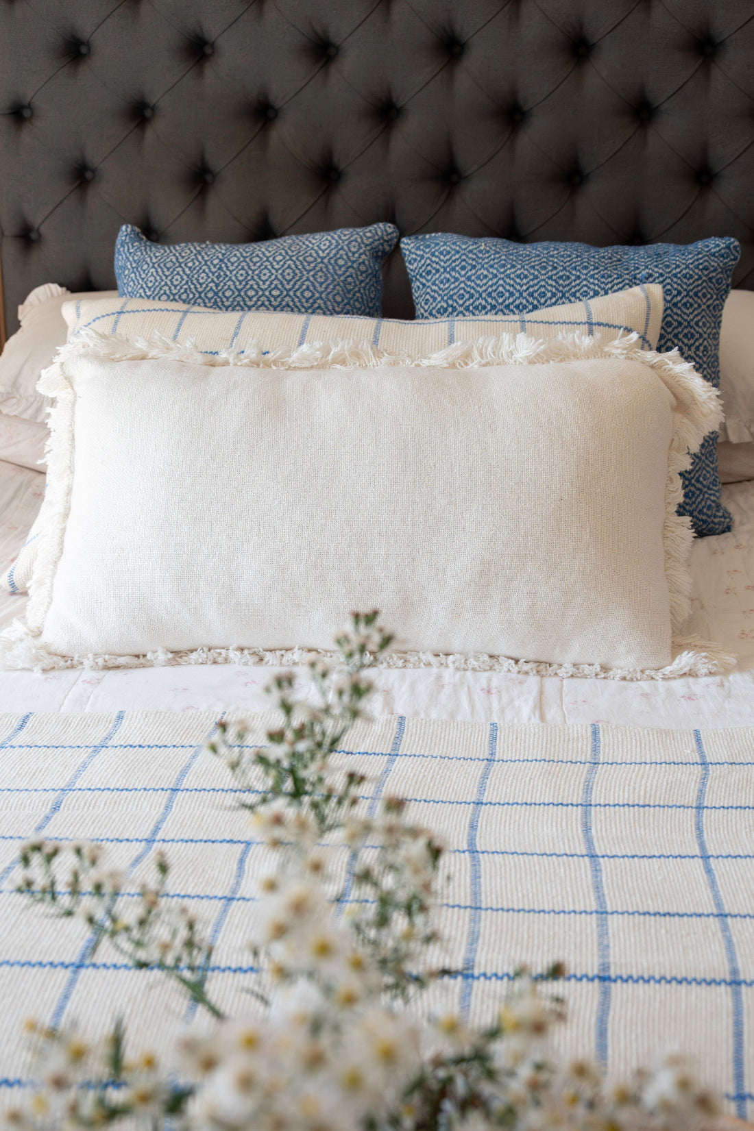 Close-up of a bed with white and blue checkered blanket, pillows, and a tufted headboard.