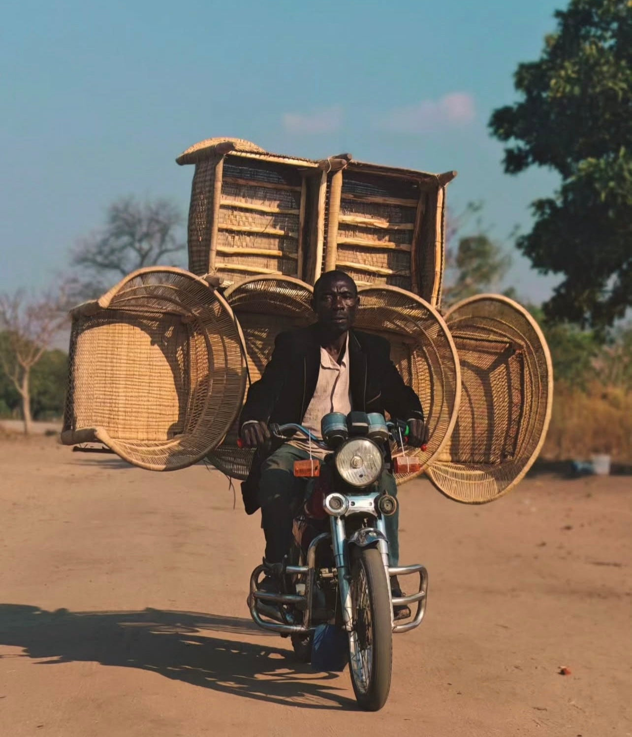 Man riding a motorcycle with Malawi chairs baskets attached on a road.