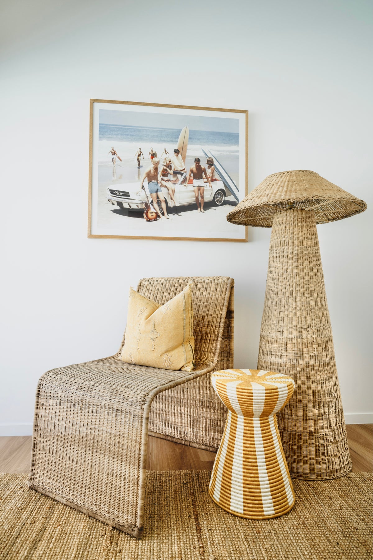 Woven chair, lamp, and stool in a room with a beach-themed painting on the wall.