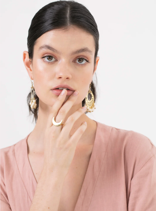 Woman wearing gold earrings and a ring, with a plain background