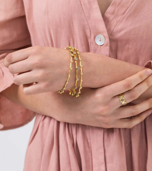 Gold bracelet and ring on a hand with a pink shirt