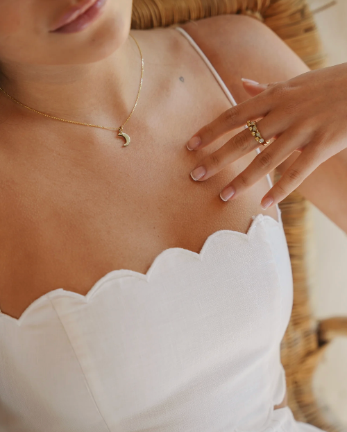 Close-up of a person wearing gold jewelry including a necklace, ring, and bracelet.
