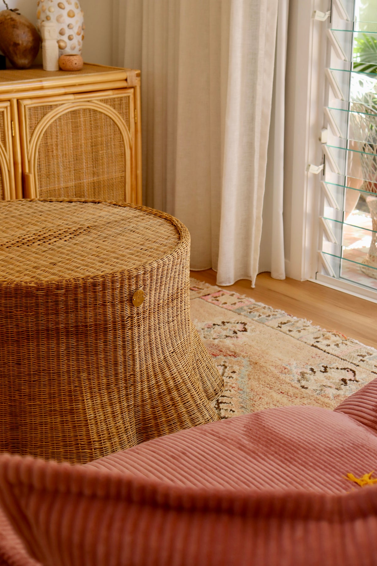 Wicker stool and pink chair in a room with curtains and a cabinet.